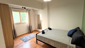 Une chambre à coucher avec un lit, une fenêtre avec des rideaux, un luminaire au plafond et un plancher en bois.