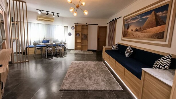 Un salon moderne avec un sol carrelé foncé, un canapé bleu agrémenté de coussins à motifs, un buffet en bois et un grand tableau représentant un paysage désertique, accroché au mur.