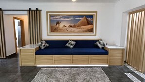 Un salon moderne avec un canapé bleu, un tableau encadré représentant une pyramide et une petite table d’appoint en bois.