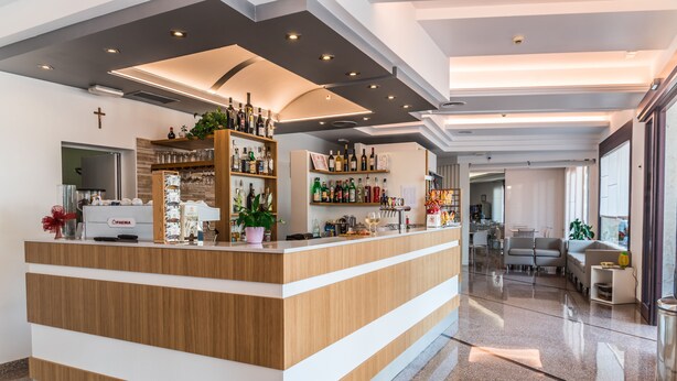 A modern reception area with a wooden counter, shelves with various items, and a cross on the wall. - Hotel Residence Mara (Jesolo)
