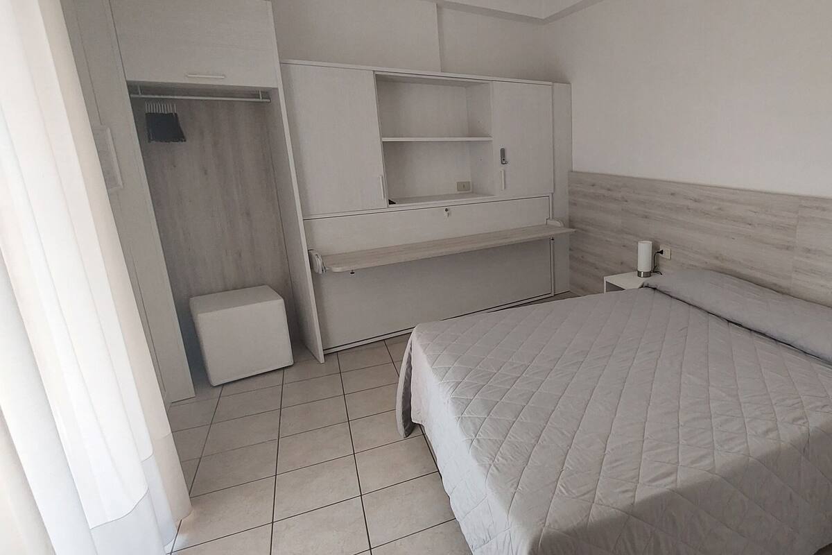 A bedroom with a bed, a nightstand, a wardrobe, and a small table.