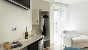 A modern hotel room with a kitchenette, a seating area with a white sofa, a small TV mounted on the wall, and a balcony with a view. - Hotel Residence Mara (Jesolo)