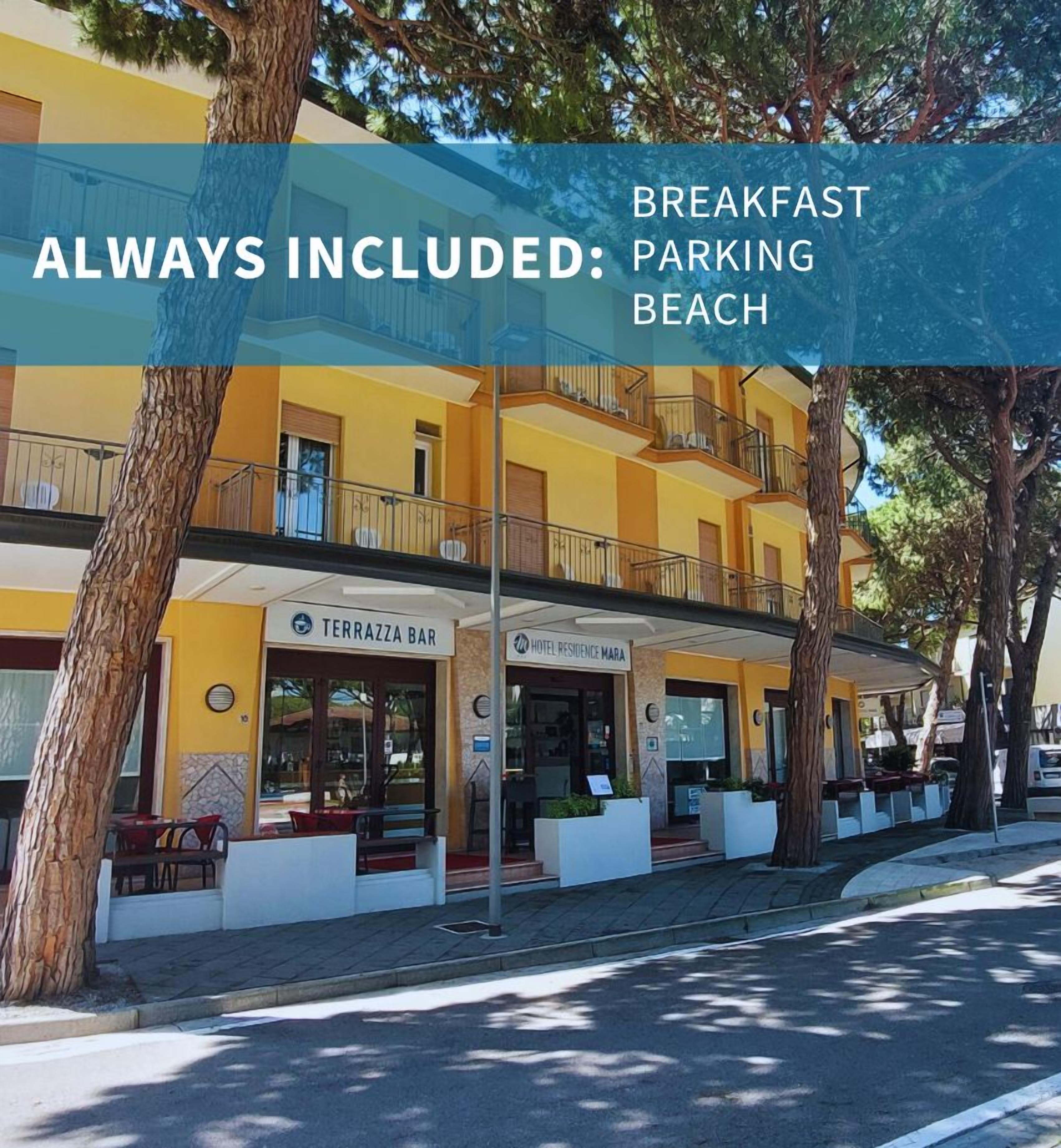 A hotel with a yellow facade, a terrace bar, and a sign indicating breakfast, parking, and beach amenities.