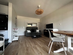 A modern living room with a sofa, coffee table, TV, and dining area.