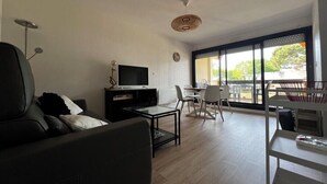 Una sala de estar moderna con sofá, televisor, mesa de comedor, sillas y un ventanal grande.