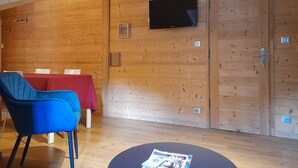 A room with wooden walls, a TV mounted on the wall, a table with chairs, and a blue chair.
