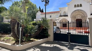 Una iglesia blanca con techo de tejas rojas, una entrada con reja y una palmera al frente.