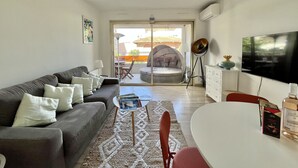 Una sala de estar con sofá, mesa de centro y televisor. Cuenta con un balcón con mesa y sillas.