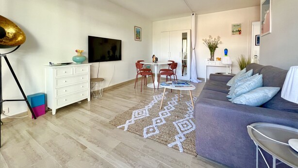 Una sala de estar moderna con un televisor de pantalla plana, un sofá, una mesa de centro y un comedor con sillas y una mesa.