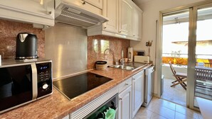 Una cocina moderna con electrodomésticos de acero inoxidable, encimera de mármol y puerta corredera de vidrio que da a una zona de estar exterior.