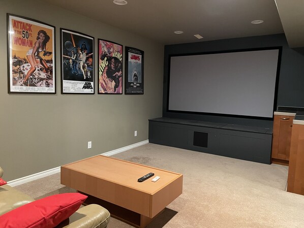 Una sala de cine en casa con una pantalla grande, una mesa de centro de madera y un sofá.