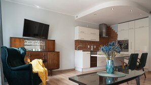 Una sala moderna con una mesa de centro de vidrio, un sillón azul oscuro y un mueble de madera con copas de vino.