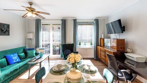 Una sala de estar moderna con un sofá verde, una mesa de comedor para dos personas, un ventilador de techo y un televisor montado en la pared.