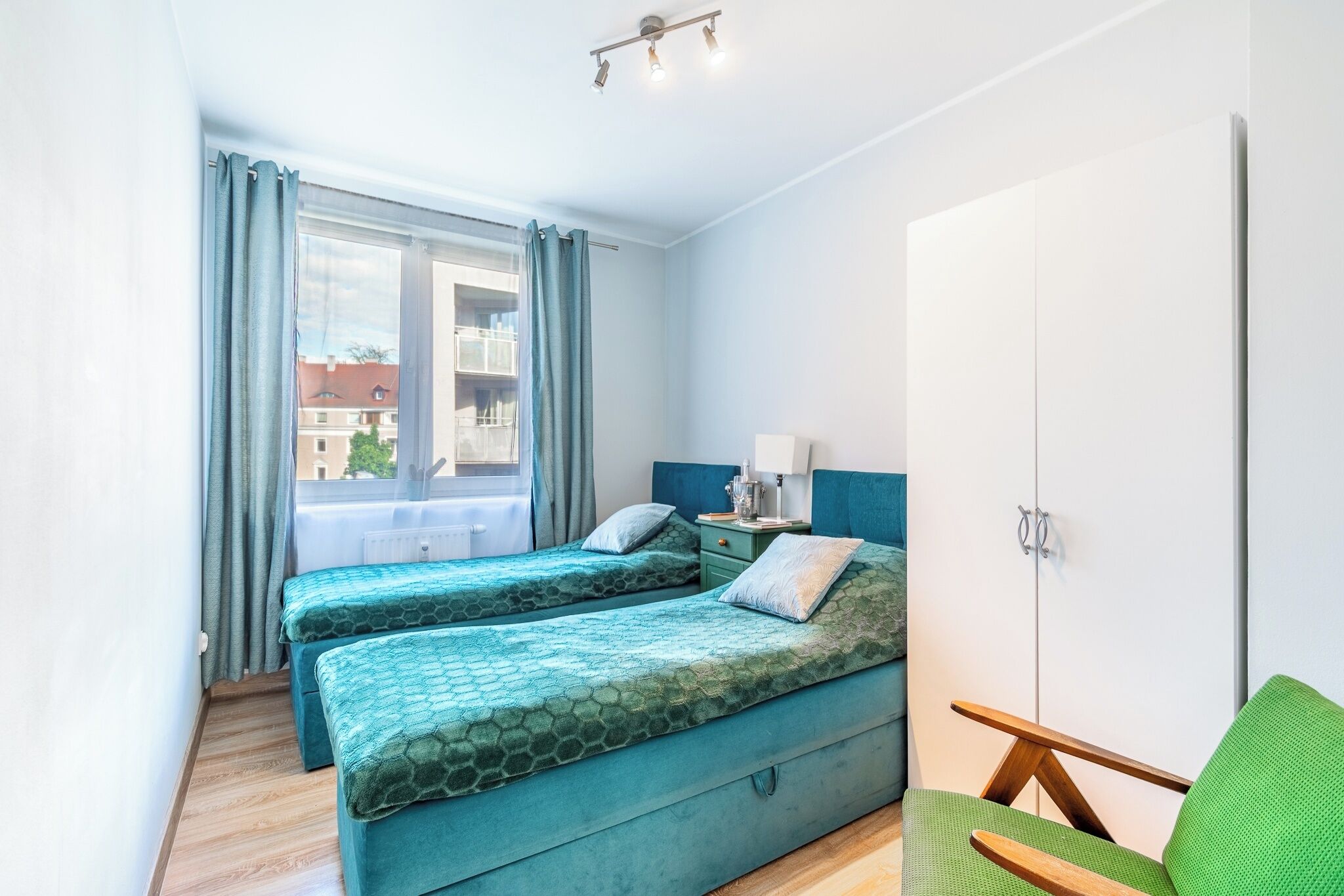 Ein Zimmer mit zwei Betten, einem Fenster mit Vorhängen, einem Kleiderschrank und einem Stuhl.