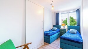 Un dormitorio con dos camas, una silla verde y una ventana con cortinas.