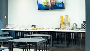Een moderne vergaderruimte met een lange tafel gedekt voor een vergadering, voorzien van diverse cateringunits en een groot scherm waarop een landschapsbeeld wordt getoond.