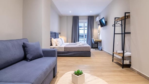 Een moderne hotelkamer met een bank, een bed, een bureau en een aan de muur bevestigde televisie.