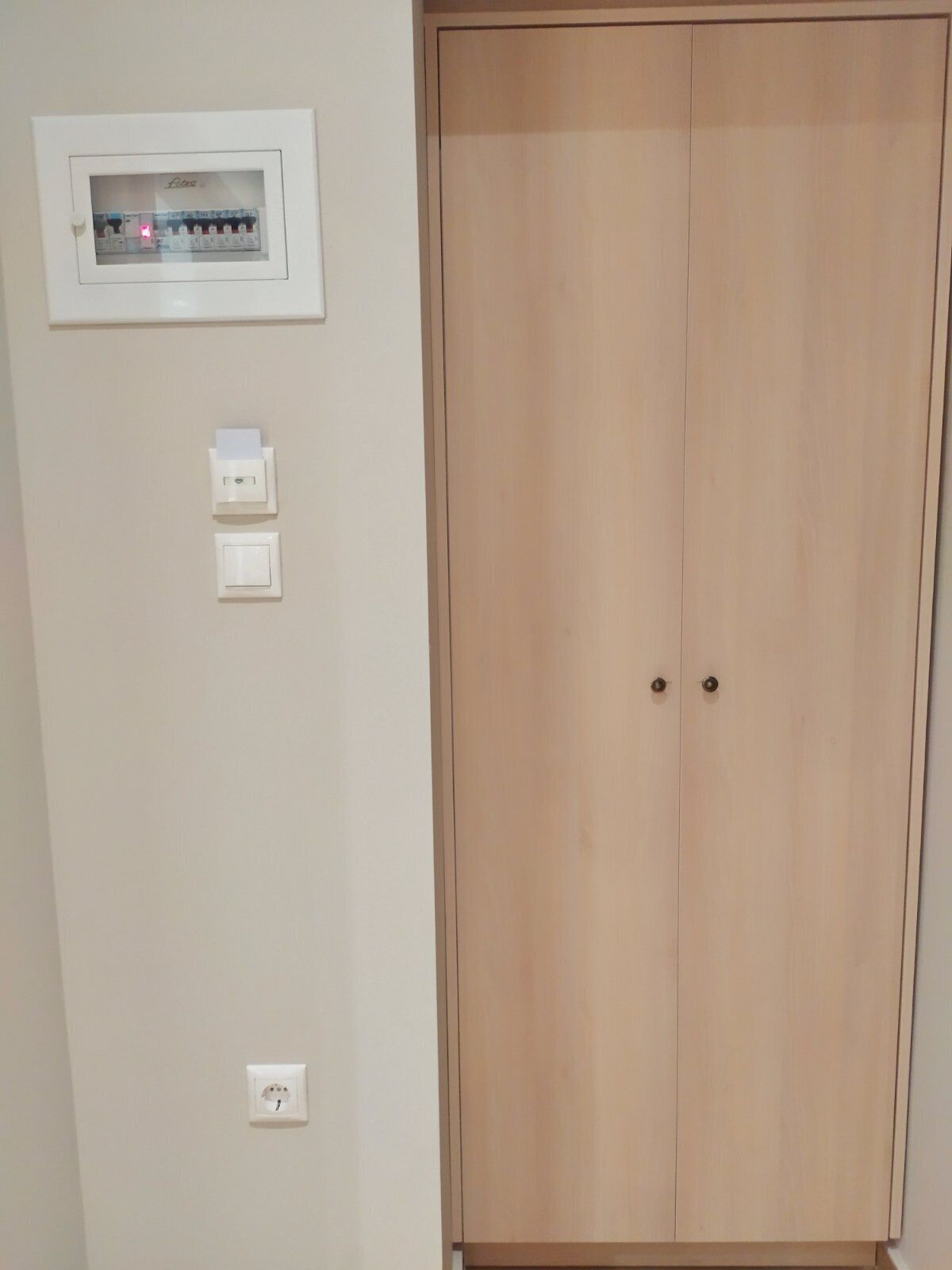 A room with a wooden wardrobe, a wall-mounted electrical outlet, and a light switch.