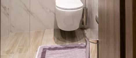 Un baño moderno con pared de mármol, inodoro, bidé y un pequeño cubo de basura.