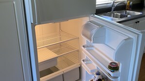 Uma geladeira branca com freezer integrado, um dispensador de água e um frasco de ketchup na prateleira da porta.