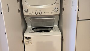 Máquina de lavar e secar frontal compacta, branca e com painel de controle, situada em uma lavanderia pequena e fechada com piso de madeira.