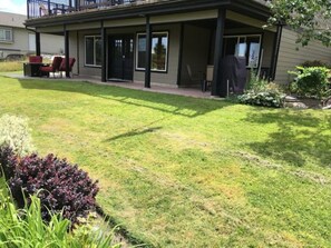 A two-story house with a covered patio area, a lawn, and a small garden with various plants.