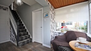 Una habitación acogedora con una escalera, un sofá, una mesa con una taza y un ventanal con vistas.