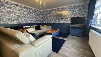 A modern living room with a sofa, a coffee table, a TV, and a patterned wall.