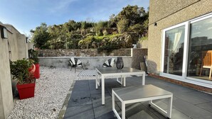 Un patio al aire libre con muro de piedra, dos mesas y sillas.