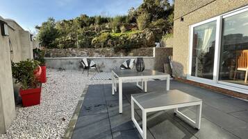 An outdoor patio with a stone wall, two tables, and chairs.