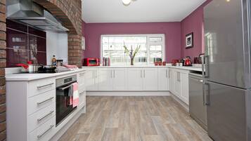 A modern kitchen with white cabinets, a stainless steel refrigerator, and a brick oven.