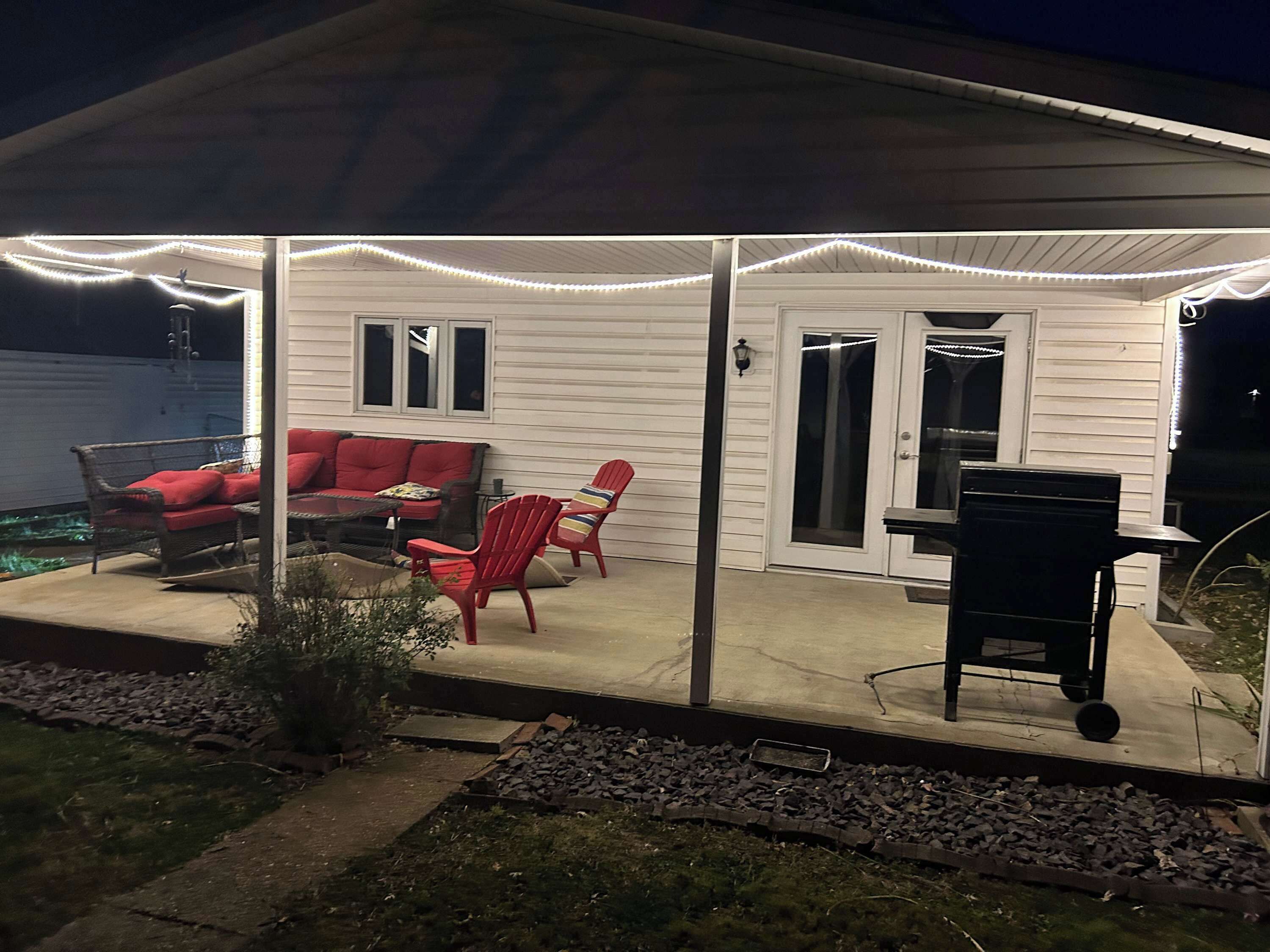 A covered patio with outdoor furniture, a grill, and string lights.