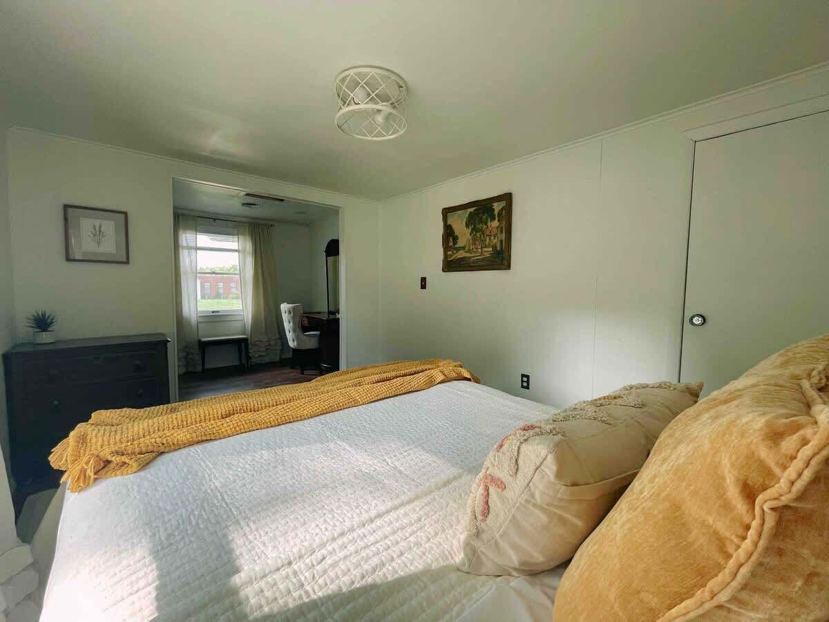 A bedroom with a bed, a dresser, a chair, a painting, and a door.