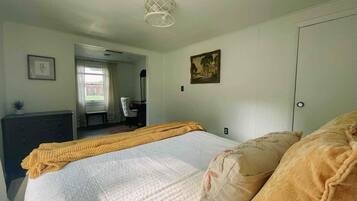 A bedroom with a bed, a dresser, a chair, a painting, and a door.