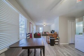 A spacious living area with a dining table, a sofa, a ceiling fan, and a laundry machine.