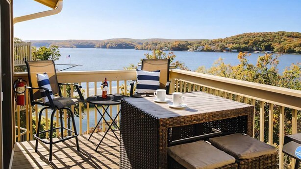 Un balcón con vistas a un lago, muebles de mimbre y una pequeña mesa con tazas.