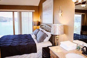 Ett hotellrum med en säng, en sänglampa, ett badrum med handfat och ett stort fönster med utsikt över en sjö eller ett annat vattendrag.