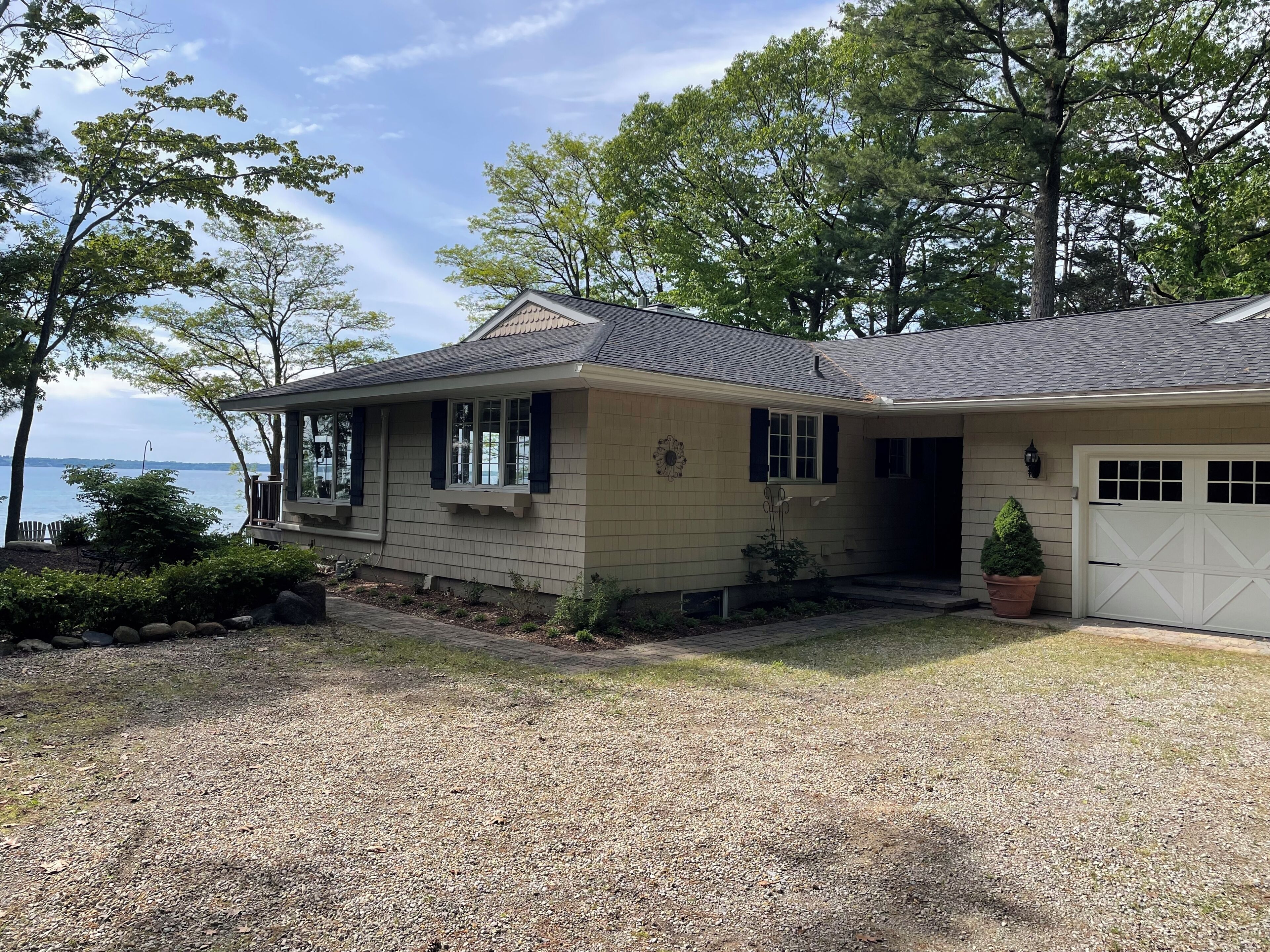A single-story house with a gravel driveway, a garage, and a view of the water.