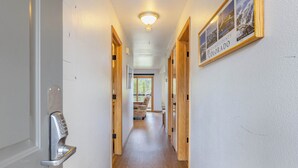 A hallway with a modern door lock, wooden doors, a framed photo of Colorado landscapes, and a rug on the floor. - Panoramic Mountain Views/Hot Tub Access/Private Deck with Grill (Keystone)