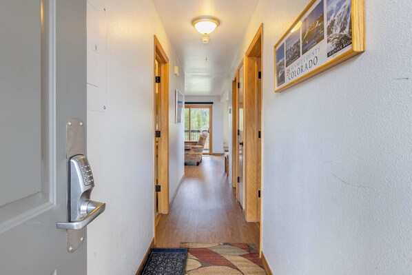 A hallway with a modern door lock, wooden doors, a framed photo of Colorado landscapes, and a rug on the floor. - Panoramic Mountain Views/Hot Tub Access/Private Deck with Grill (Keystone)