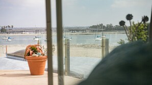 Blick aus einem Fenster auf einen Strand mit Booten, einer Brücke und einem Blumentopf im Fensterbrett.