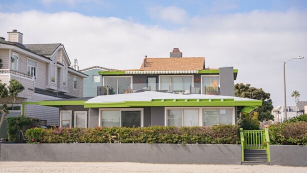 Ein modernes, zweistöckiges Haus mit Flachdach, großen Fenstern und einer grünen Veranda.