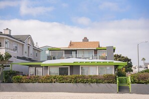 Ein modernes, zweistöckiges Haus mit Flachdach, großen Fenstern und einer grünen Veranda.