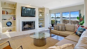 A modern living room with a fireplace, a large flat-screen TV mounted on the wall, and a sofa with decorative pillows. - Baybreeze-3bd, 2ba, sleep 8 (San Diego)