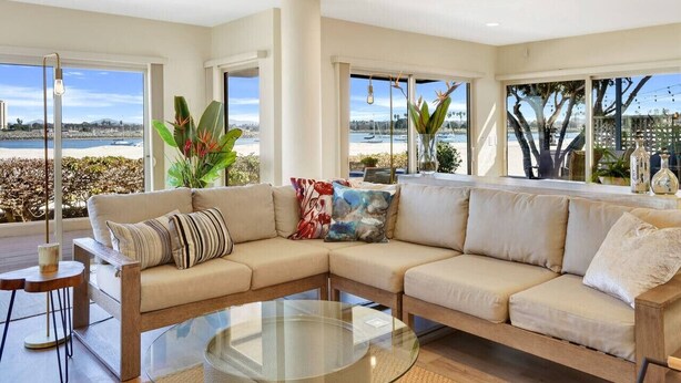 A spacious living room with a beige sectional sofa, a glass coffee table, and large windows offering a view of the beach. - Baybreeze-3bd, 2ba, sleep 8 (San Diego)