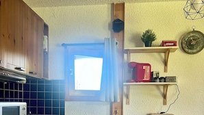 Une cuisine compacte avec des meubles en bois, un four à micro-ondes, une poubelle rouge et une petite table avec des tabourets.