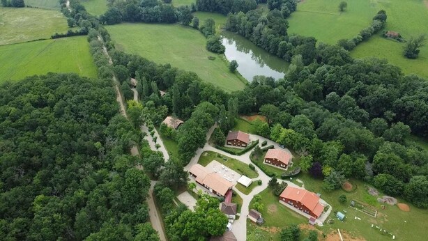 Vista aérea de una propiedad rural con un estanque, rodeada de exuberante vegetación y dos edificios principales con tejados rojos.