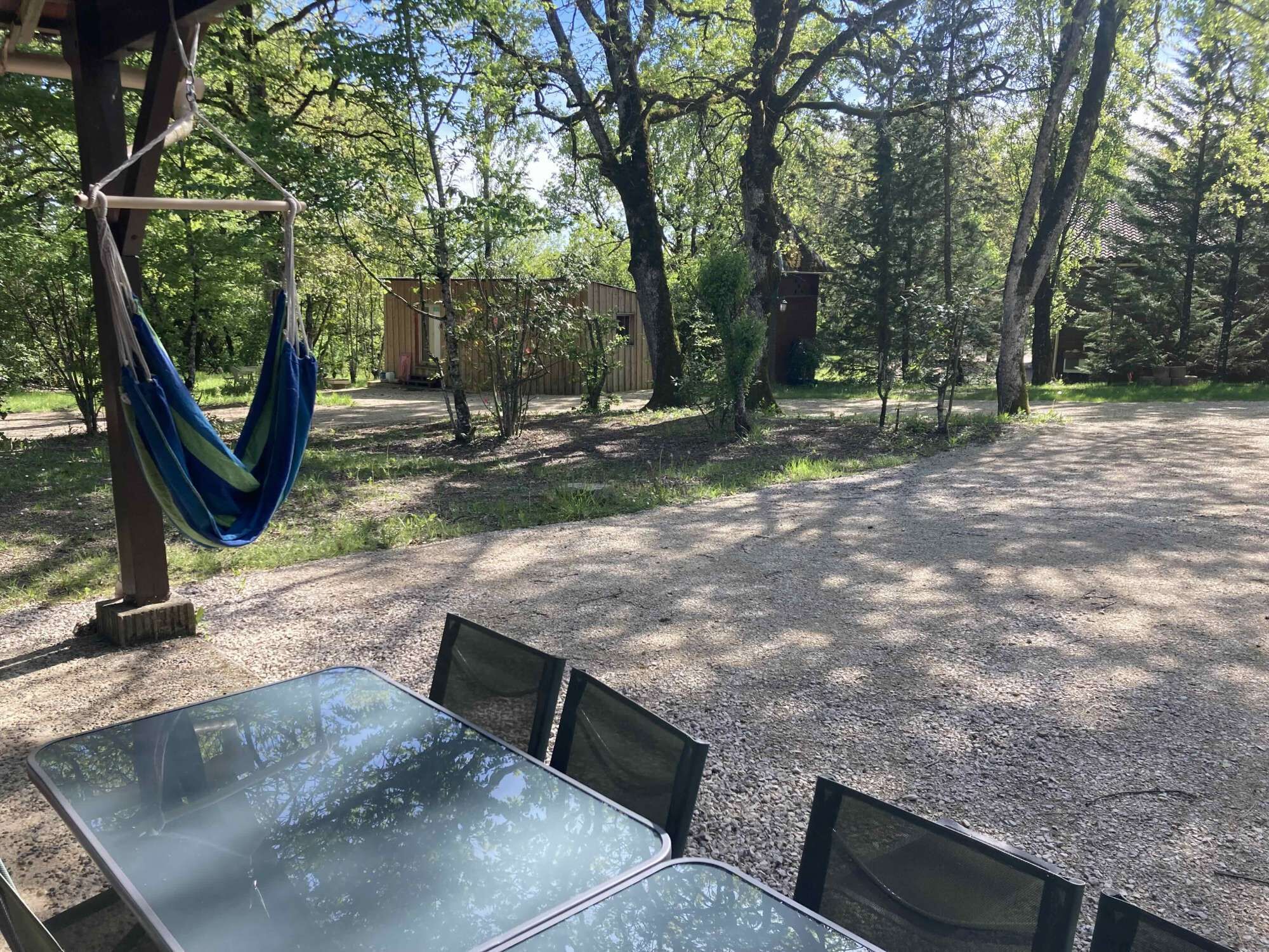 Un espacio de descanso al aire libre con techo, una mesa, sillas, árboles y una hamaca.