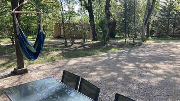 Un espacio de descanso al aire libre con techo, una mesa, sillas, árboles y una hamaca.