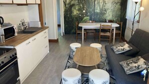Un espacio habitable compacto con kitchenette, zona de comedor y rincón de estar con sofá y otomanas.